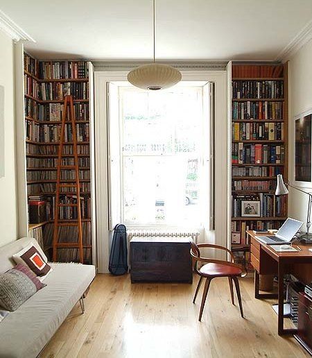 a living room filled with furniture and bookshelves next to a window covered in lots of books