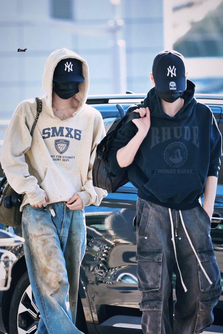 two young boys walking down the street in front of a car wearing hoodies and sweatshirts