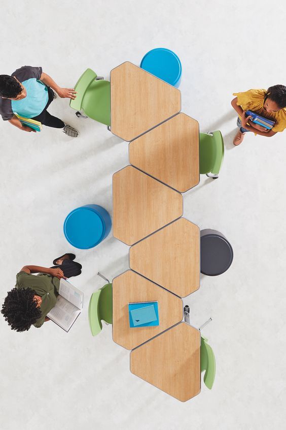 three people sitting at a table with chairs around it, looking down on their laptops