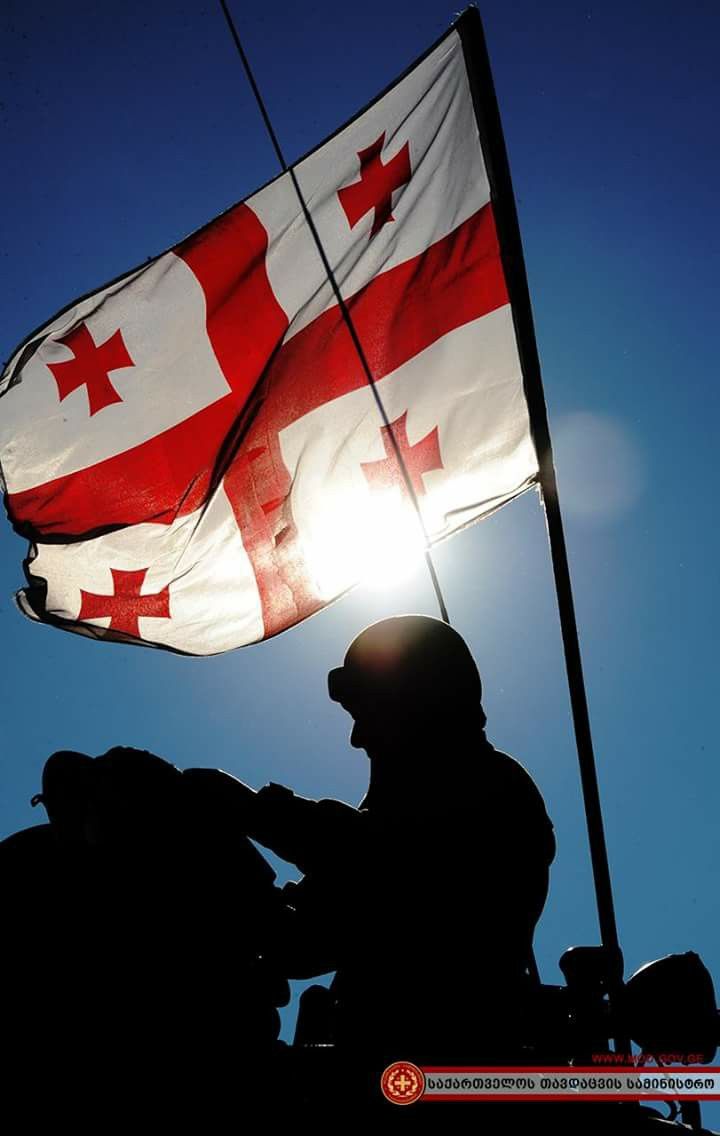 a canadian flag flying in the sky with a man sitting on a motorcycle under it