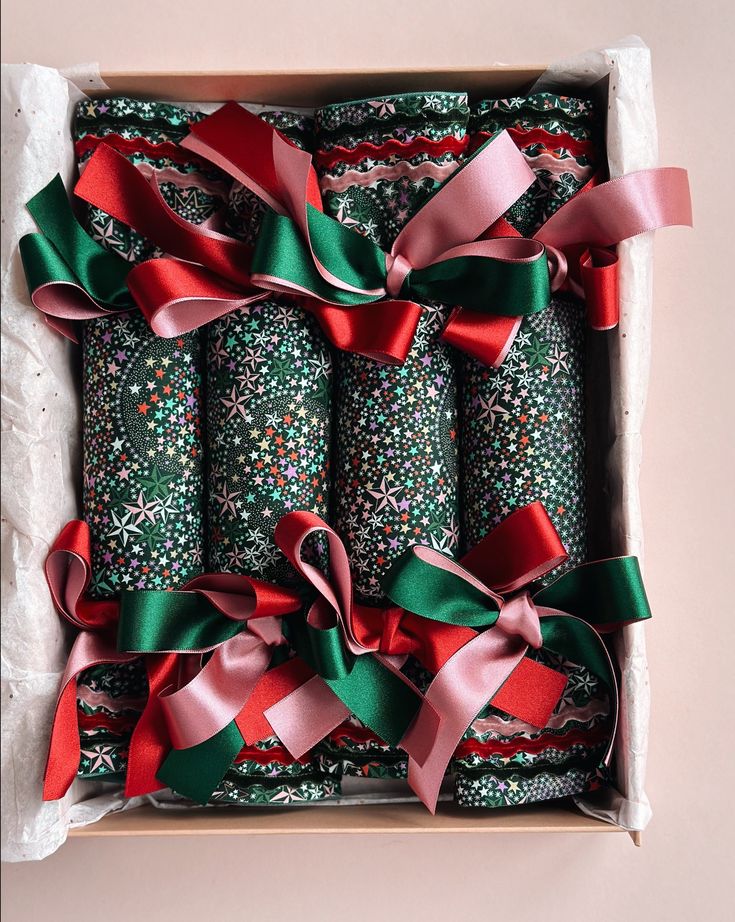 six wrapped christmas crackers in a gift box with ribbons and bows on the top