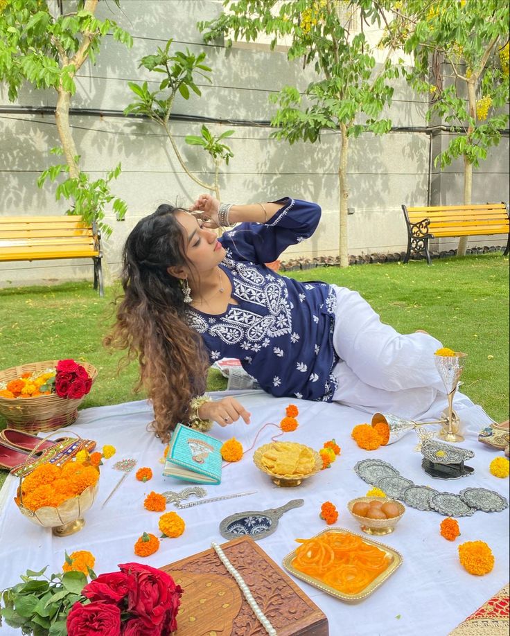 a woman laying on top of a table covered in orange and yellow flowers next to cakes