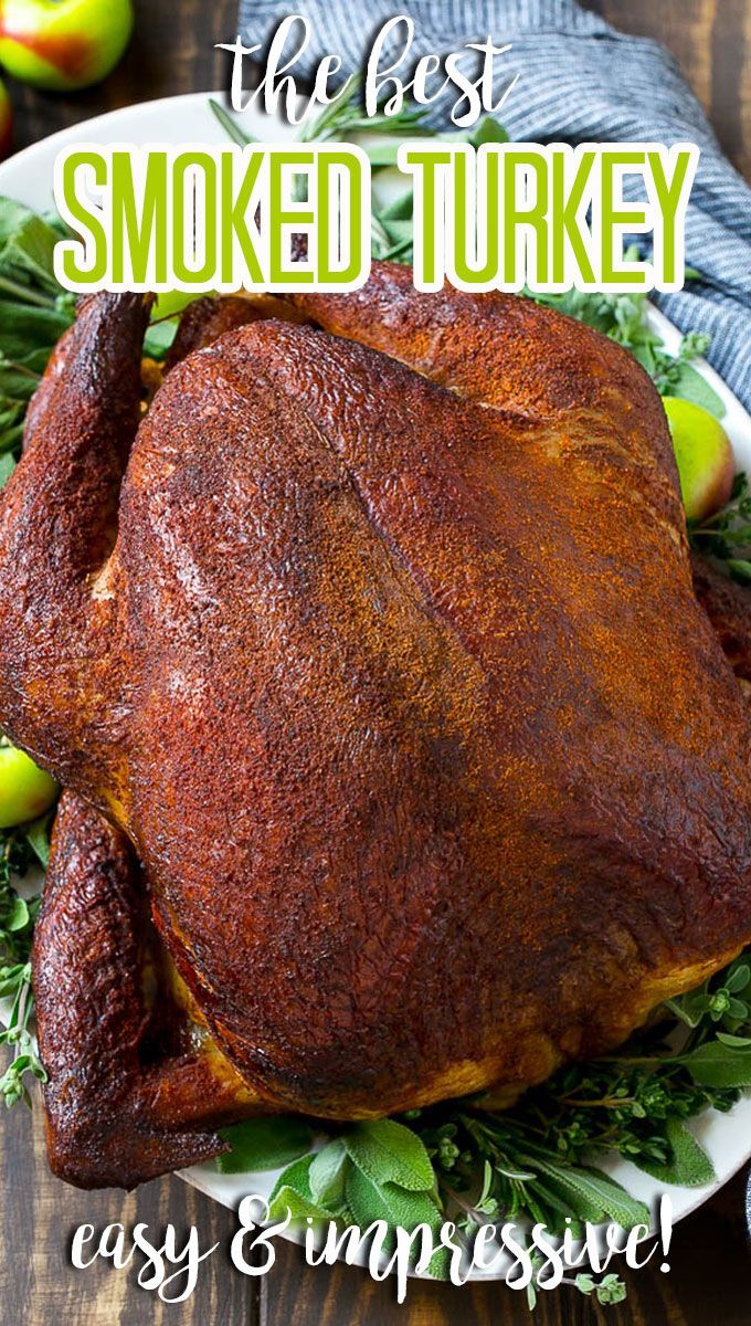 a roasted turkey on a white plate with green leaves and apples in the back ground