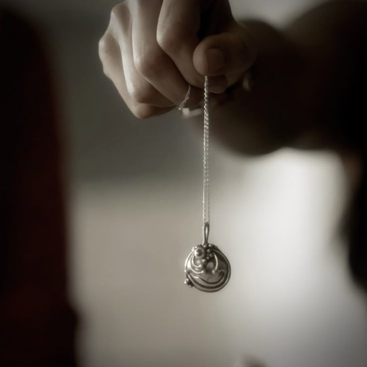 a person holding a silver necklace with a spiral design hanging from it's end