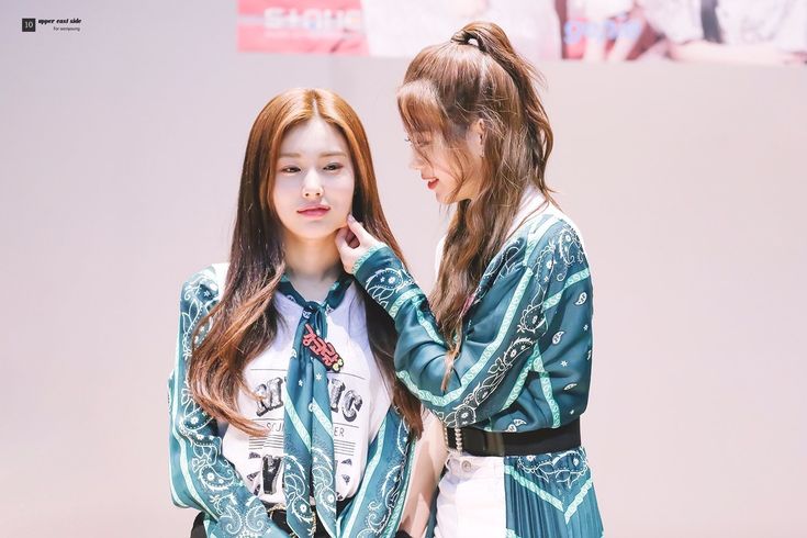 two young women standing next to each other in front of a white wall and one is touching her ear