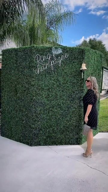 a woman standing in front of a tall green hedge with writing on it's side