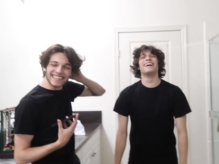 two young men standing in front of a bathroom mirror, one smiling and the other laughing