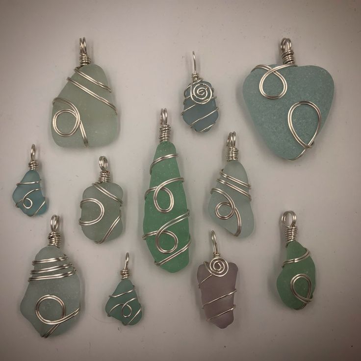 nine different sea glass pendants are displayed on a white surface with silver wire around them