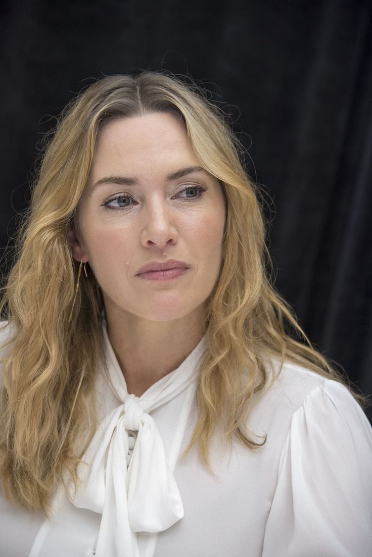 a woman with long blonde hair wearing a white shirt and posing for a photo in front of a black background