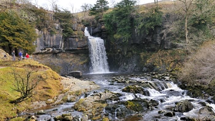 people are standing at the base of a waterfall