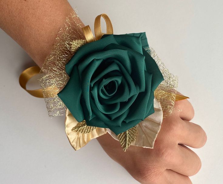 a person's hand holding a green rose with gold leaves and lace on it