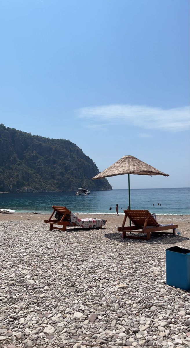 two lounge chairs and an umbrella on the beach with mountains in the backgroud