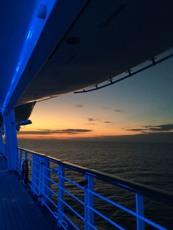 the deck of a ship at sunset with blue lights on it and water in the background