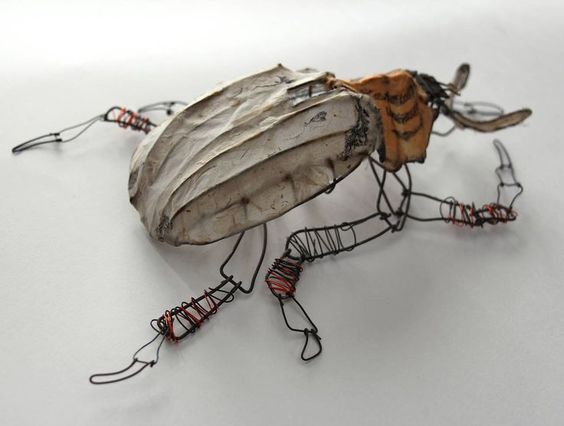 a wire sculpture of a bug on a white surface with red and black wires around it