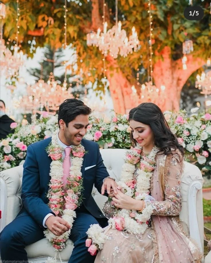 a man and woman sitting on top of a couch next to each other in front of flowers