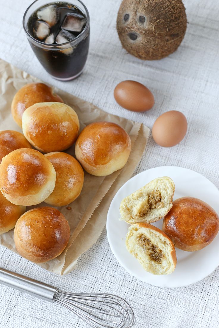 several rolls on a plate next to some eggs and an egg in a glass cup