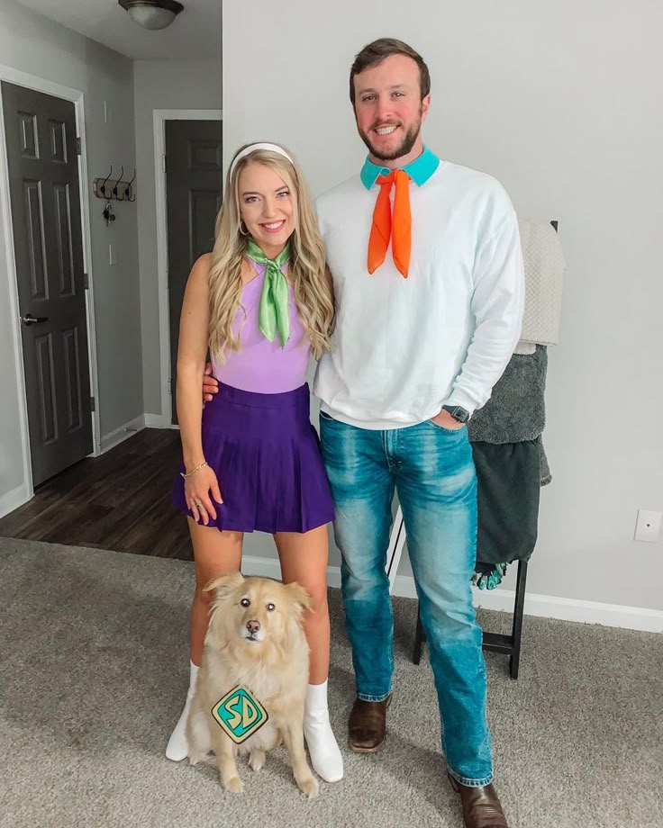 a man and woman standing next to a dog in front of a white wall with an orange ribbon on it