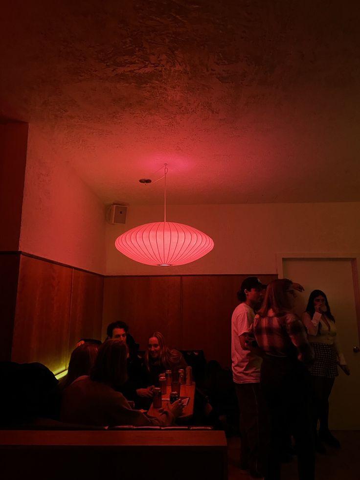 some people are sitting in a room with red lights on the ceiling and one person is standing up