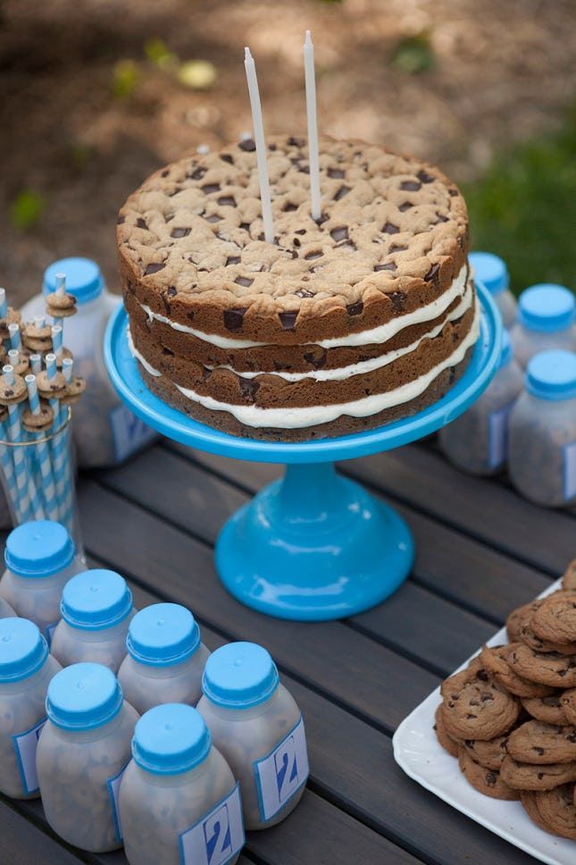 a cookie cake and cookies on a table with bottles of milk, candles and desserts