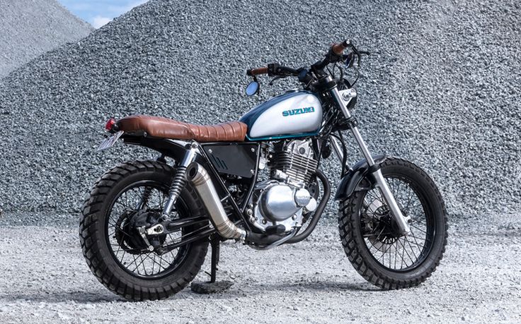 a white and black motorcycle parked in front of a large pile of gravel with mountains in the background