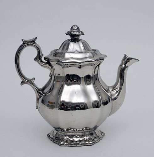 a silver teapot with a lid and handle on it's side, sitting against a white background