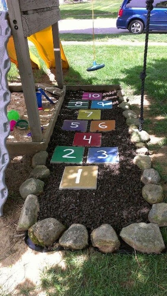 a child's play area with rocks and numbers on the ground next to a swing set