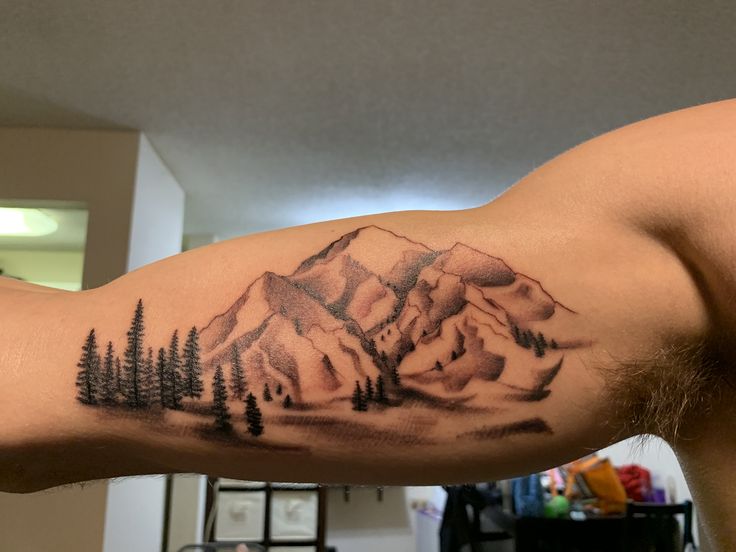 a man's arm with a mountain and pine tree tattoo on the upper half of his arm