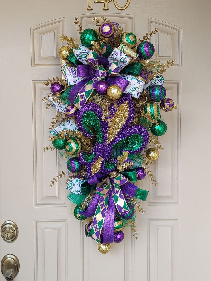 a purple and green christmas wreath hanging on the front door to a white door with numbers forty