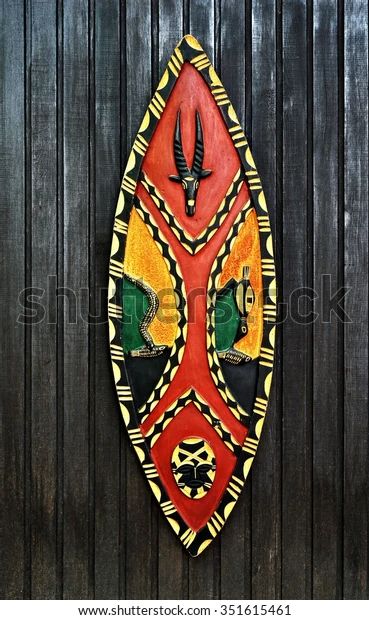 an african mask hanging on the side of a wooden door in front of a green wall