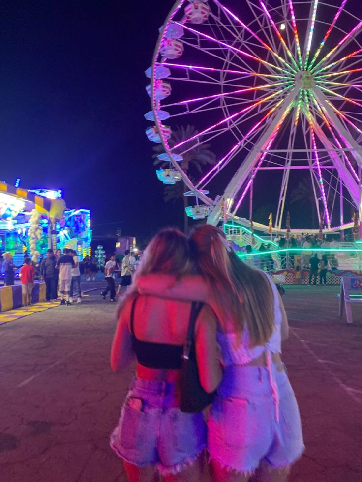 two girls hugging in front of a ferris wheel