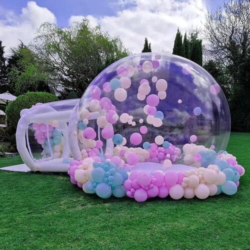 an inflatable bubble filled with pink, blue and white balloons sitting on top of a lush green field