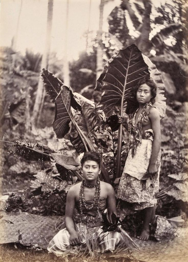 an old photo of two people standing next to each other with large leaves on their heads