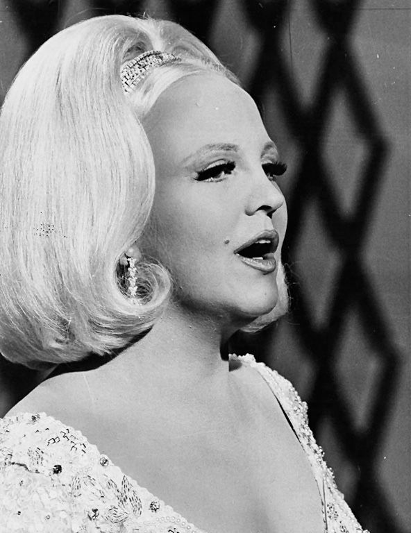 an old photo of a woman with blonde hair and big earrings on her head, in front of a chain link fence