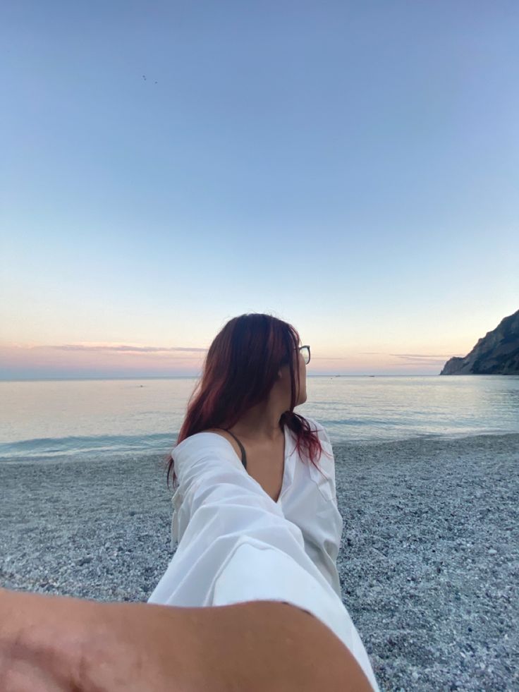 a woman sitting on top of a sandy beach next to the ocean with her legs crossed