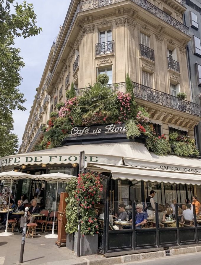 people sitting at tables in front of a building with plants growing on the side of it