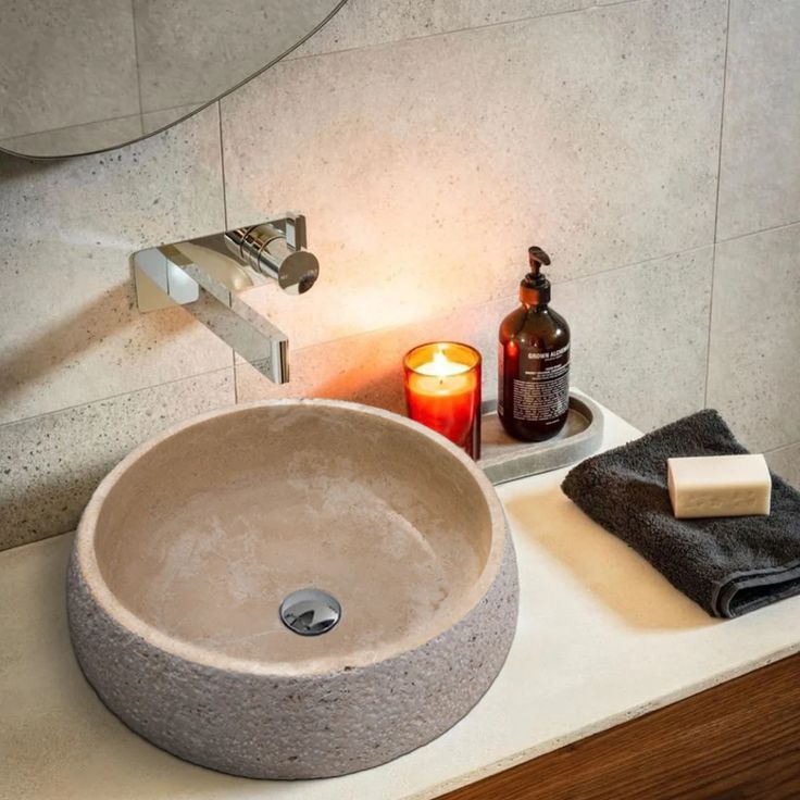 a bathroom sink sitting on top of a counter next to a candle and soap dispenser