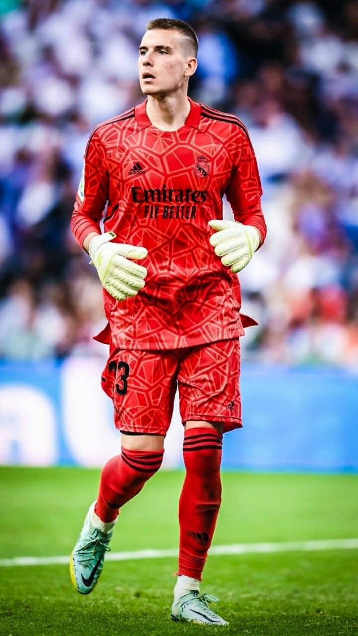 a soccer player is running on the field with his hands in his pockets and wearing white gloves