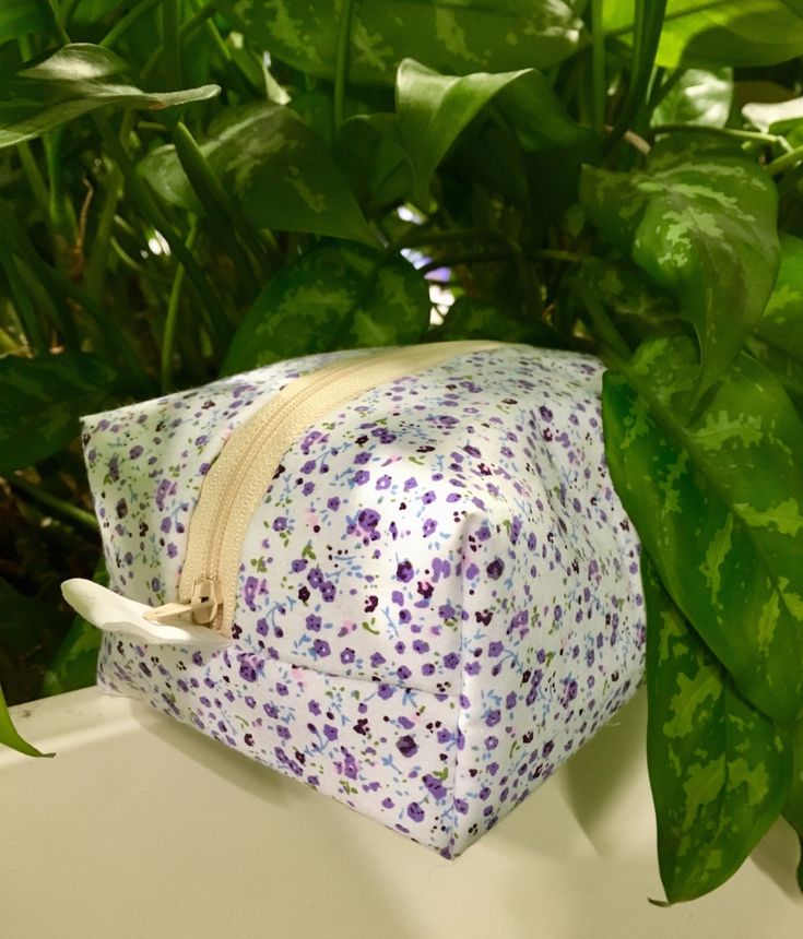 a purple and white bag sitting on top of a table next to a plant with green leaves