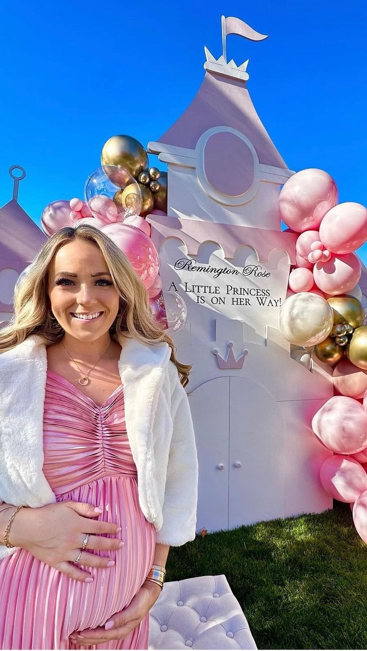 a pregnant woman standing in front of a pink and white castle with balloons on it