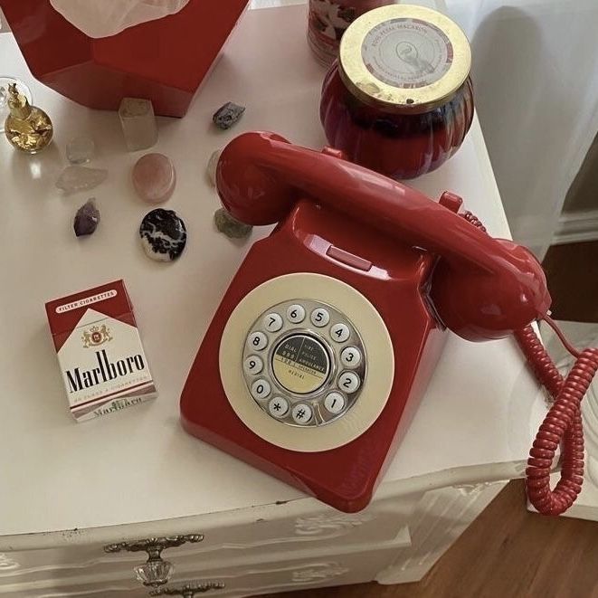 an old fashioned red phone sitting on top of a table next to other items and glassware