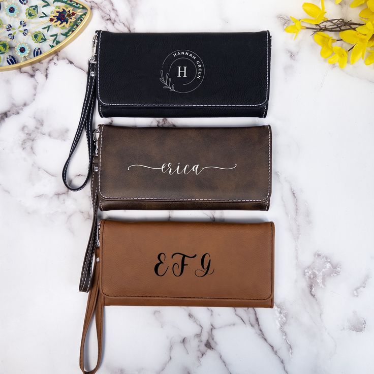 three personalized leather wallets on a marble countertop with flowers in the background