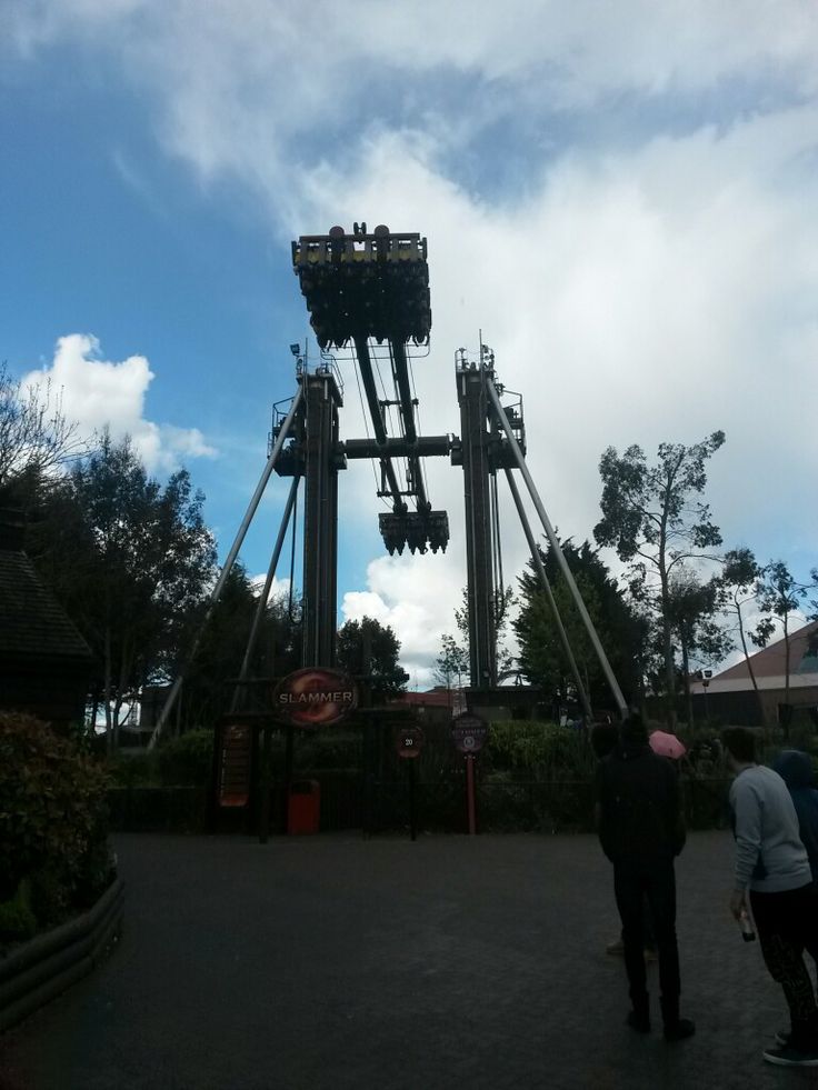 two people are standing in front of a roller coaster at an amusement park on a cloudy day