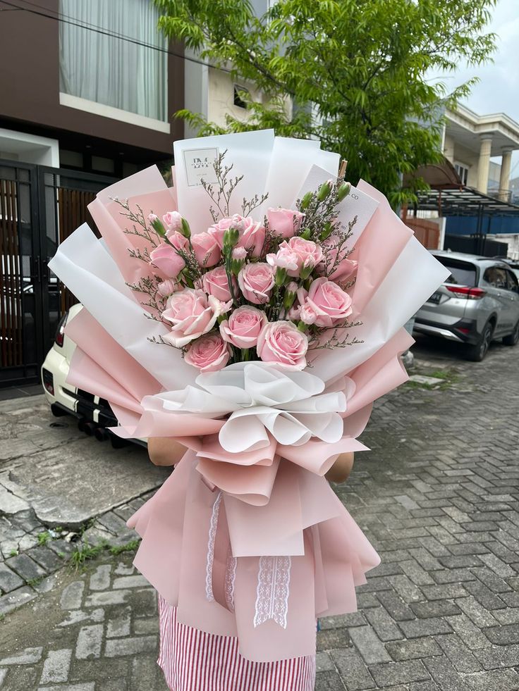 a woman holding a bouquet of pink roses in her hand on the sidewalk next to a building