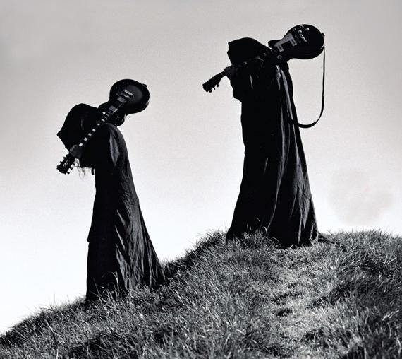 two women dressed in black standing on top of a grass covered hill next to each other