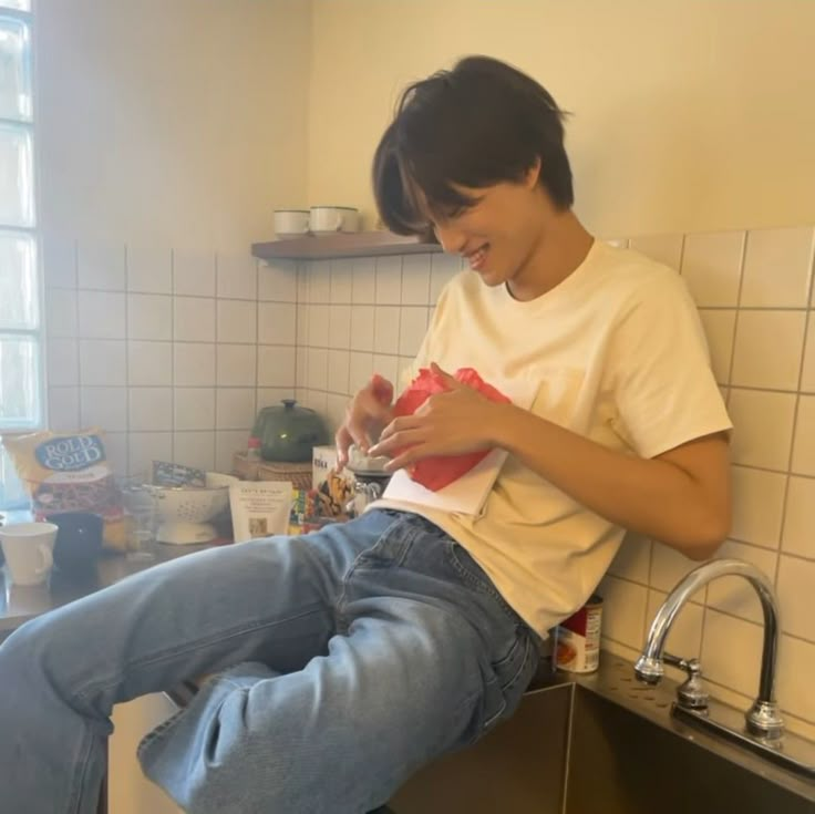 a young man sitting on top of a kitchen counter next to a faucet