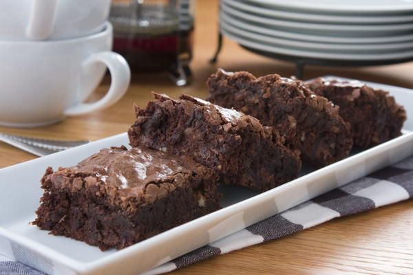 two pieces of brownie on a white plate next to some cups and saucers