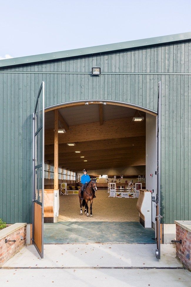 a horse is walking out of an open barn door with its rider in the saddle