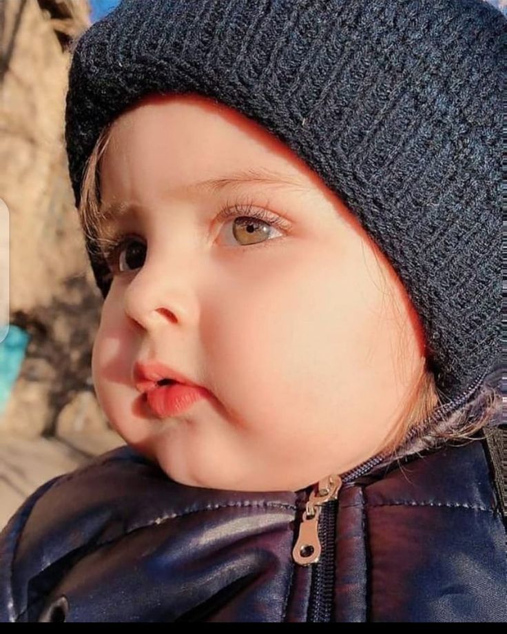 a small child wearing a knitted hat and leather jacket looking to the side with its mouth open