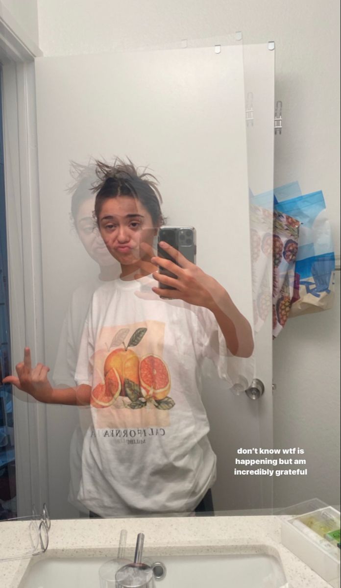 a woman taking a selfie in front of a bathroom mirror while holding a cell phone