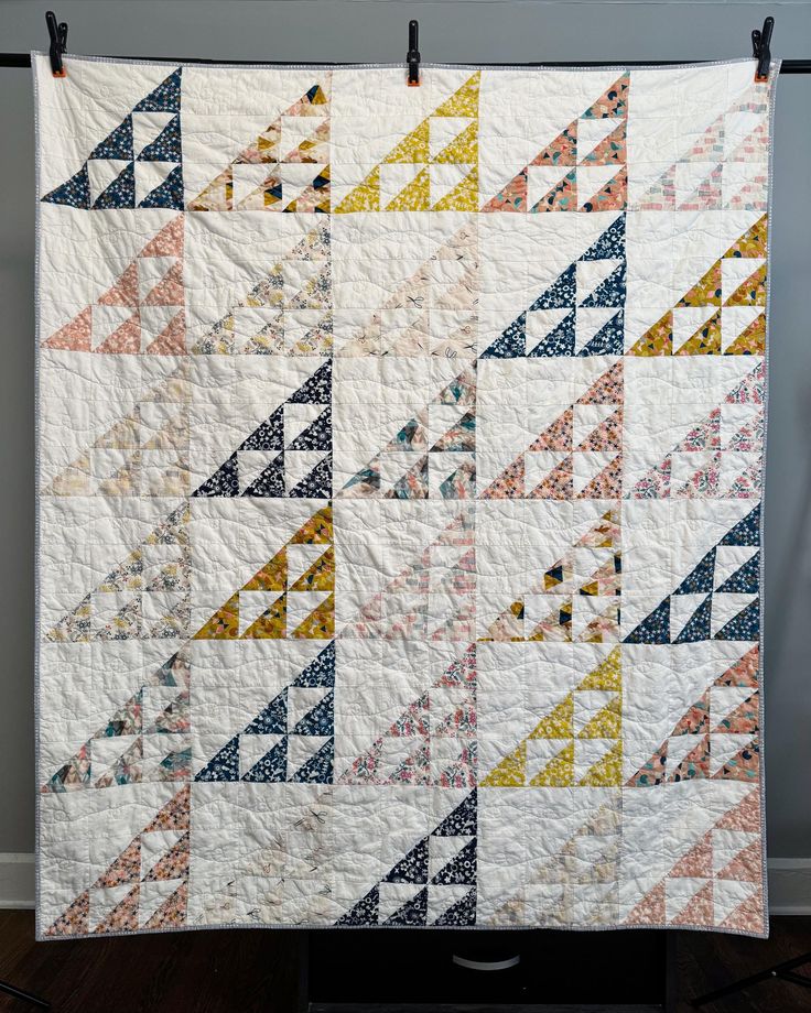 a quilt hanging on a clothes line in front of a wall with an orange, yellow and blue triangle design